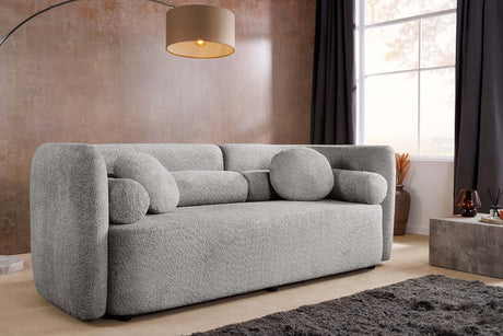 Szara sofa bouclé z zaokrąglonymi bokami i ozdobnymi poduszkami – nowoczesny mebel do eleganckiego salonu