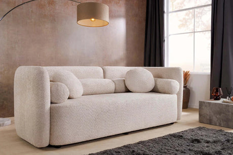 Beżowa sofa bouclé z zaokrąglonymi bokami i ozdobnymi poduszkami – nowoczesny mebel do eleganckiego salonu