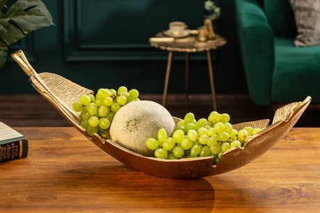 Złota metalowa misa w kształcie liścia na drewnianym stole, dekoracyjna ozdoba wnętrza