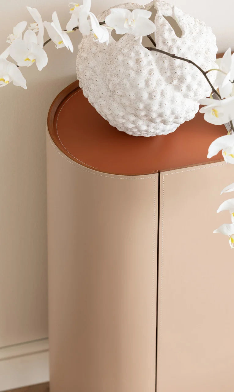 Beżowa komoda w ekoskórze na czarnych, stalowych nogach z zaoblonymi bokami i półkami w środku