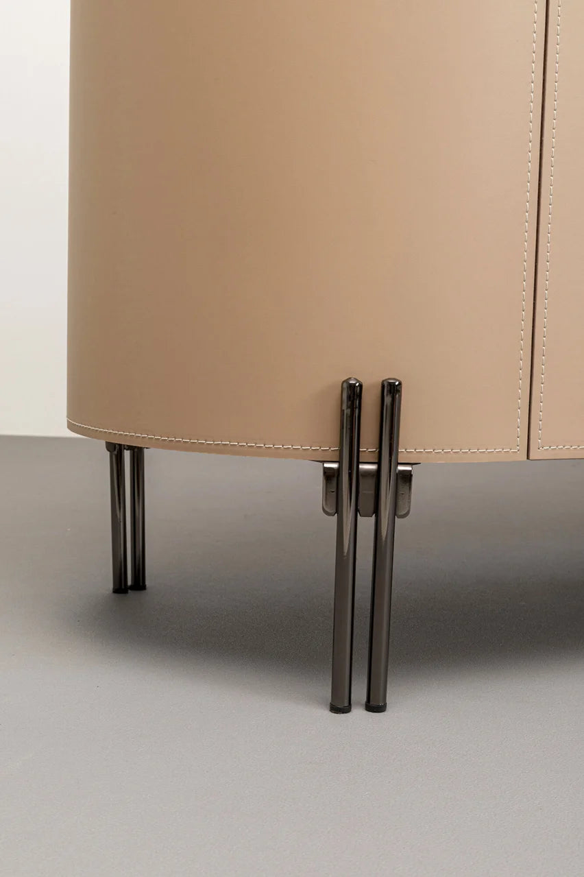 Beżowa komoda w ekoskórze na czarnych, stalowych nogach z zaoblonymi bokami i półkami w środku.