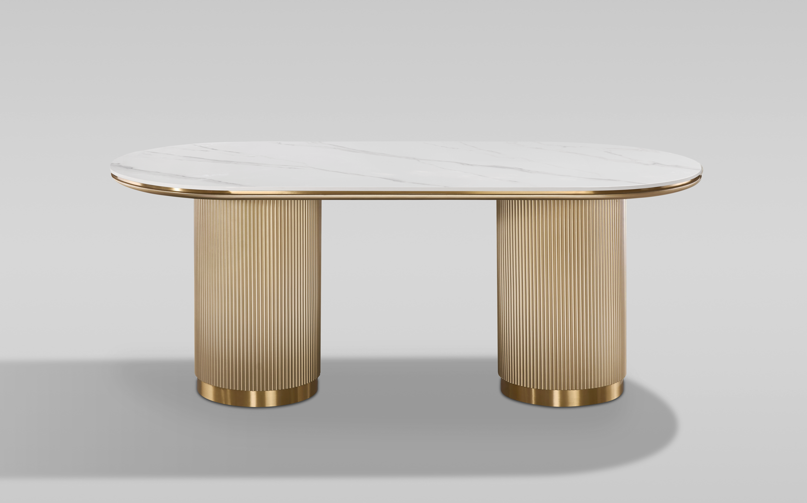 Nowoczesny stół w kolorze złota z białym owalnym blatem syntetycznym, na dwóch ryflowanych cylindrycznych nogach ze złotym wykończeniem.